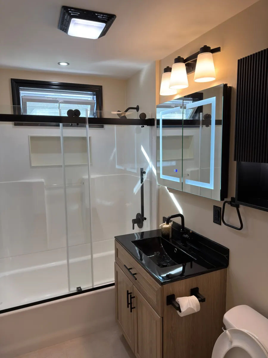 Finished bathroom with LED backlit mirror, black sink top and matte black hardware